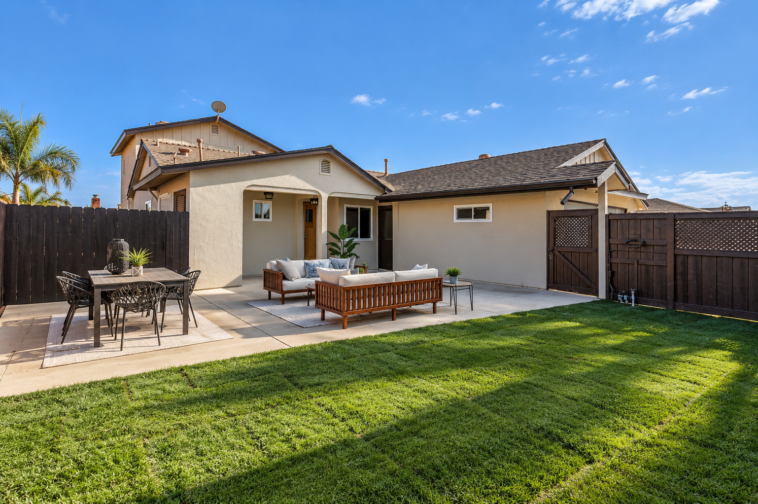 Suburban backyard landscaping with a wide green lawn, a patio dining and seating area, and a wooden fence in the San Fernando Valley