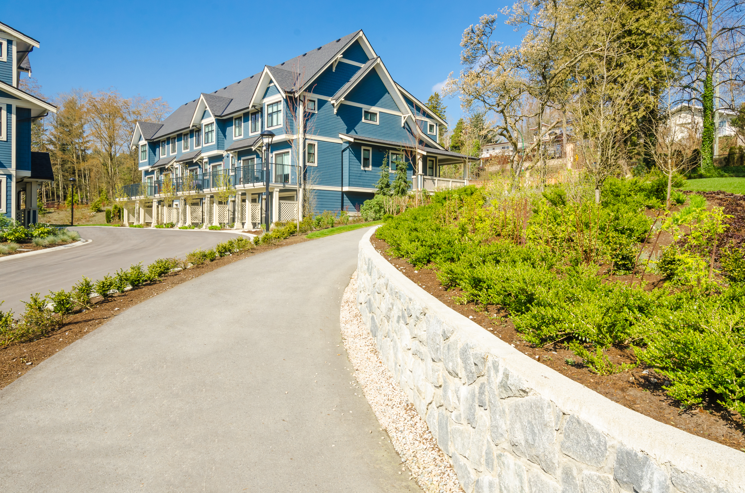 Blue suburban apartment buildings with landscaped grounds and stone retaining wall showing patio options in Sherman Oaks.