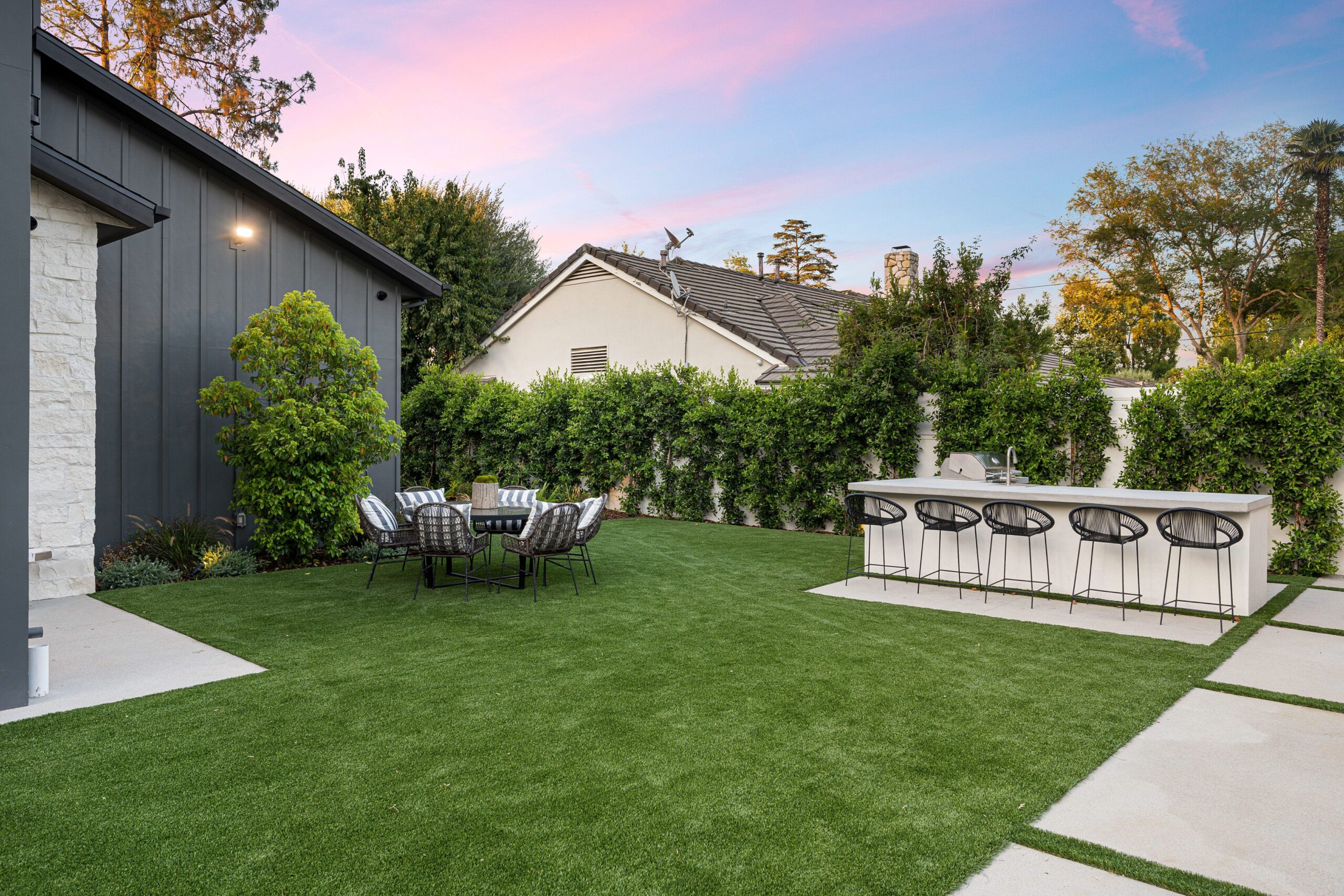 Backyard entertainment area with an outdoor dining space and bar counter at twilight, part of a hardscape design project in the San Fernando Valley
