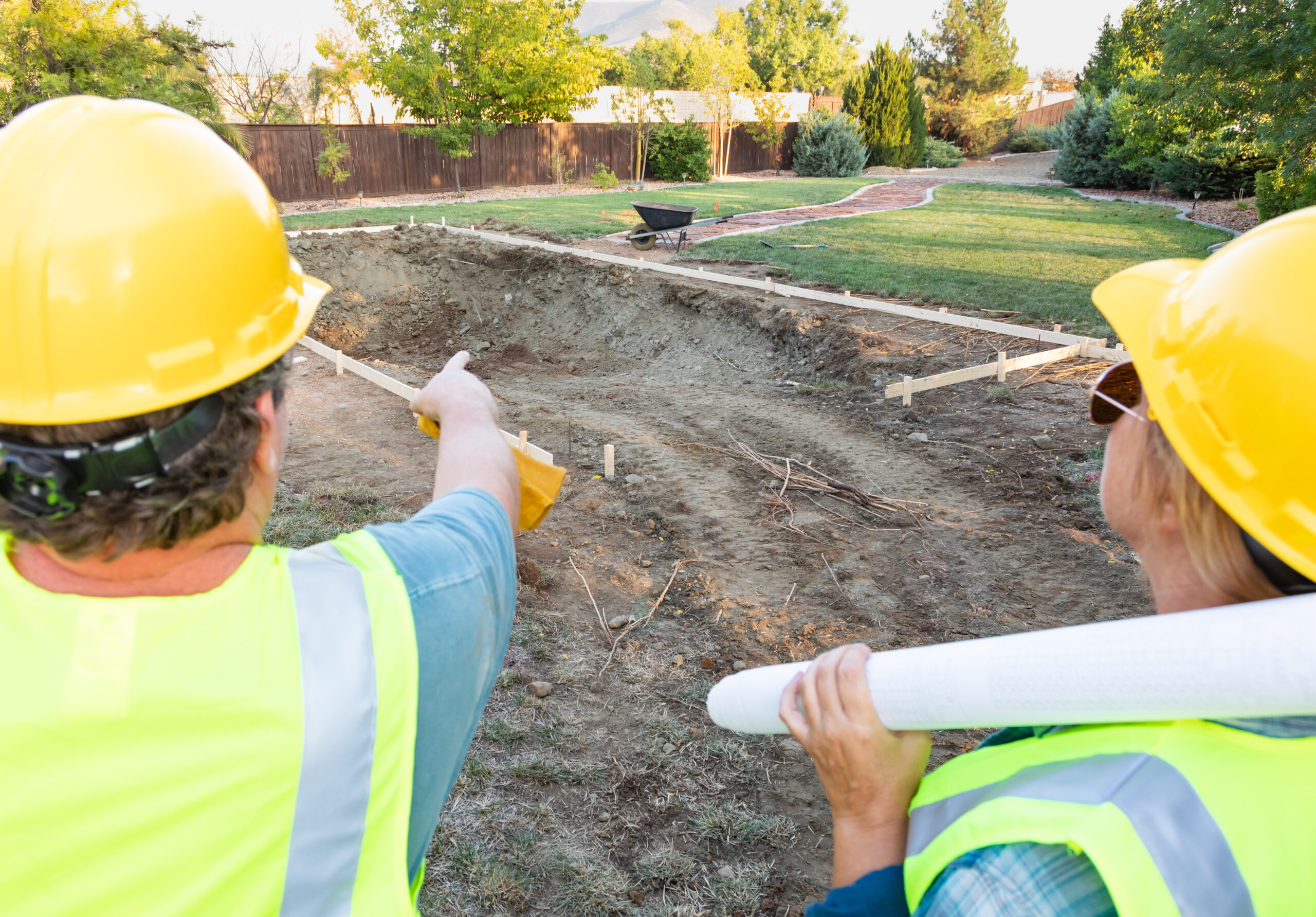 Two workers in hard hats and safety vests overlooking a staked-out excavation on a front yard landscaping project in the San Fernando Valley