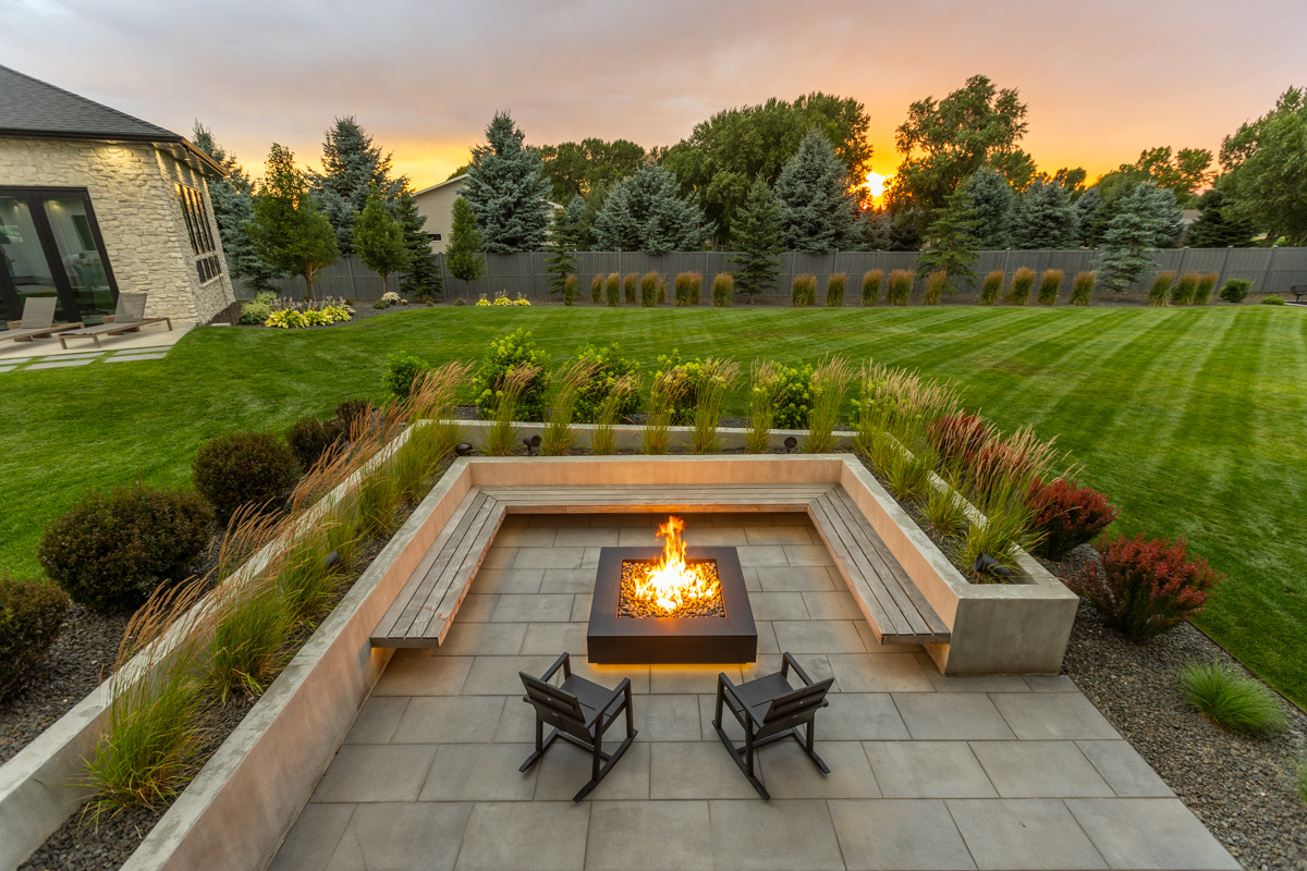 Landscape design with a curved stone patio, a fire pit, built-in seating, and raised planters beside a green lawn in the San Fernando Valley