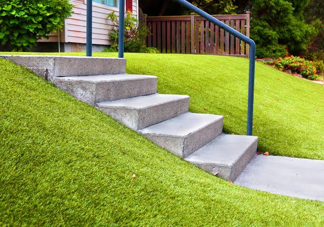 Backyard landscaping with concrete steps and a handrail climbing a grassy slope beside a house in the San Fernando Valley