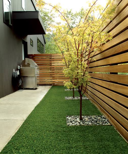 Backyard landscaping in a narrow side yard with a green lawn, small trees, and a horizontal wooden fence in the San Fernando Valley