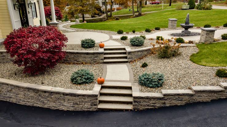 Retaining walls of stacked stone terracing a front garden with concrete steps, gravel beds, shrubs, and a fountain in the San Fernando Valley