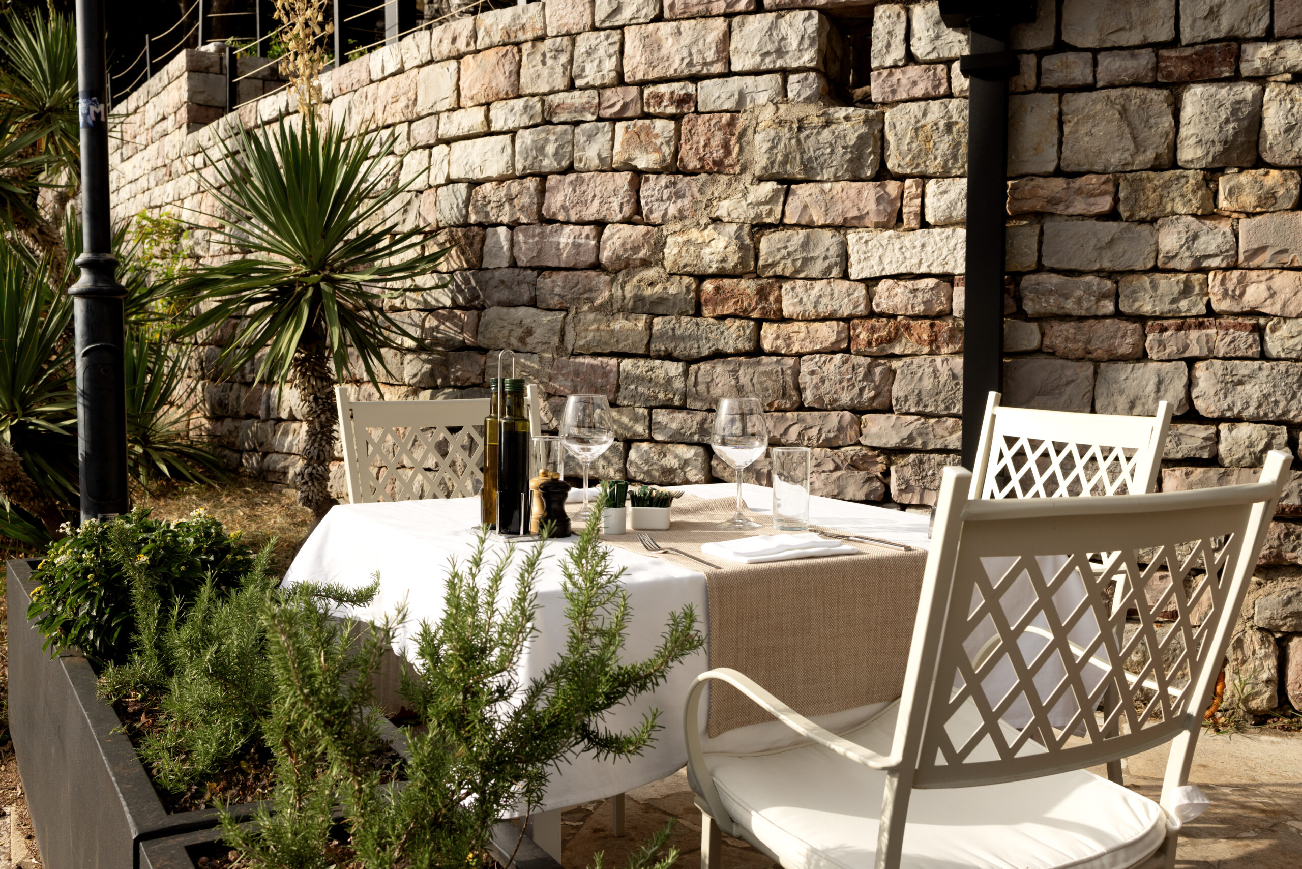 Outdoor dining table set for two beside a natural stone retaining wall and herb planters in the San Fernando Valley